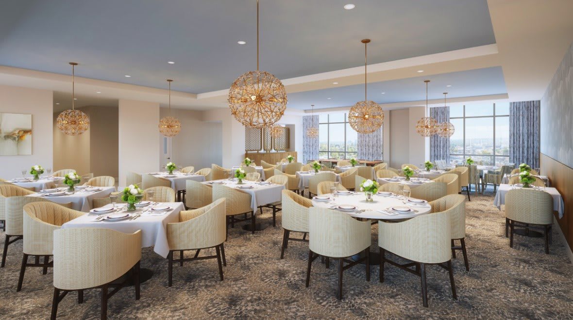 An elegant restaurant dining area with neatly arranged tables and plush chairs, illuminated by decorative chandeliers.