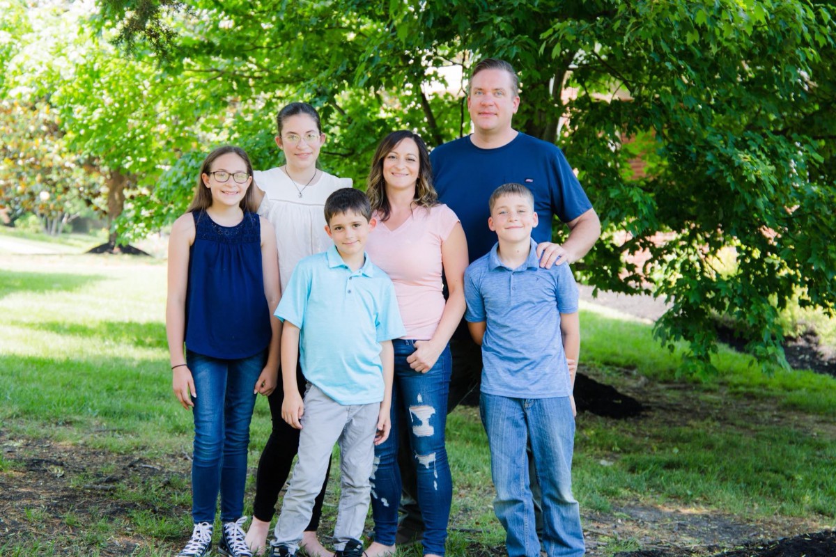 A family of six posing together in a lush green park.
