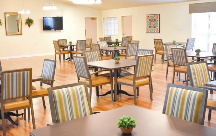 An empty dining room with neatly arranged tables and chairs, decorated with small plants and a television on the wall.
