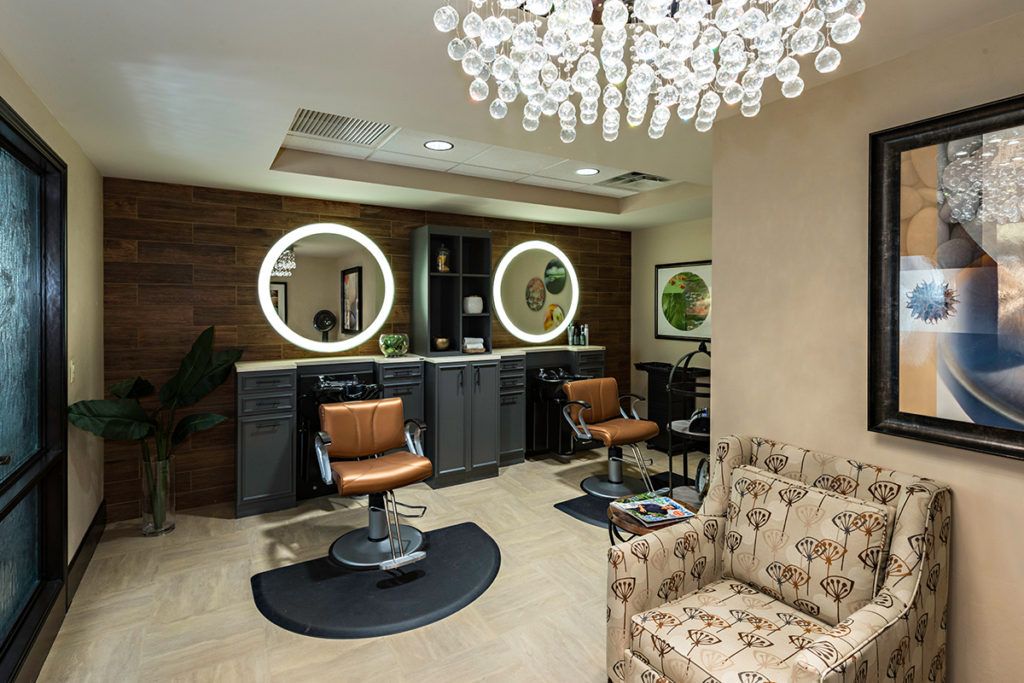 A modern salon interior featuring stylish barber chairs, illuminated mirrors, and a decorative chandelier.