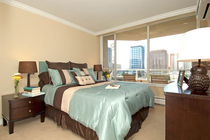A modern bedroom with elegant decor and a large window offering a city view.