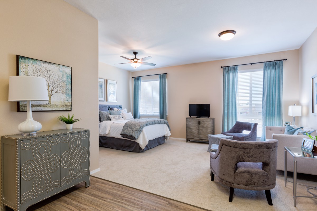 A modern bedroom with neutral tones, featuring a comfortable bed, a ceiling fan, and seating area.