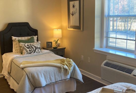 A cozy bedroom with a neatly made bed, decorative pillows, and a warm lamp on the nightstand.