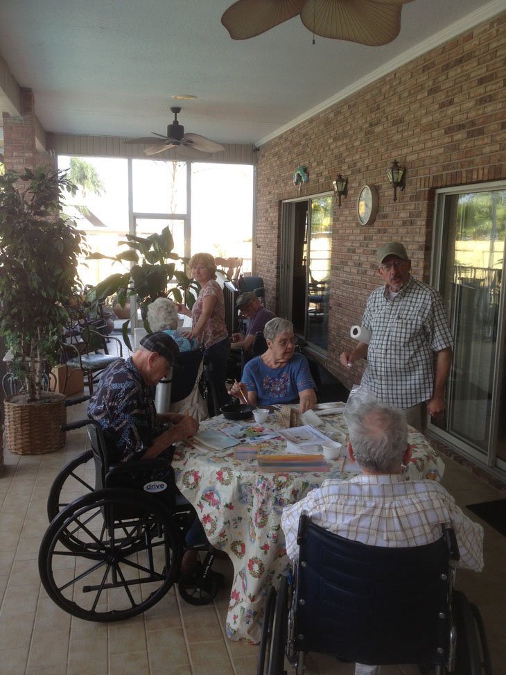 A group of seniors gathered around a table on a porch, enjoying conversation.
