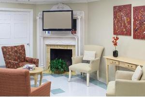 A cozy living room with a television above the fireplace, surrounded by comfortable chairs and tasteful decor.