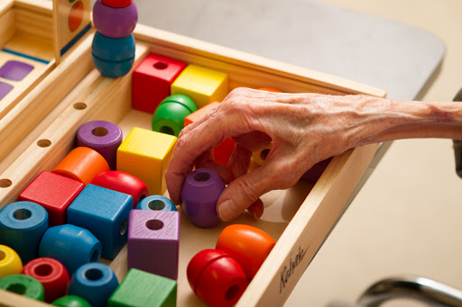 An elderly hand reaching for colorful wooden blocks in a playful learning activity.