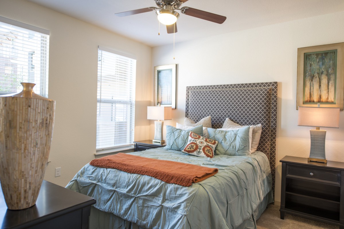 A cozy bedroom featuring a neatly made bed with decorative pillows, a bedside lamp, and natural light streaming through the window.