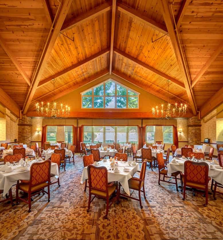 An elegant dining room with a wooden ceiling and chandeliers, set up for a fine dining experience.