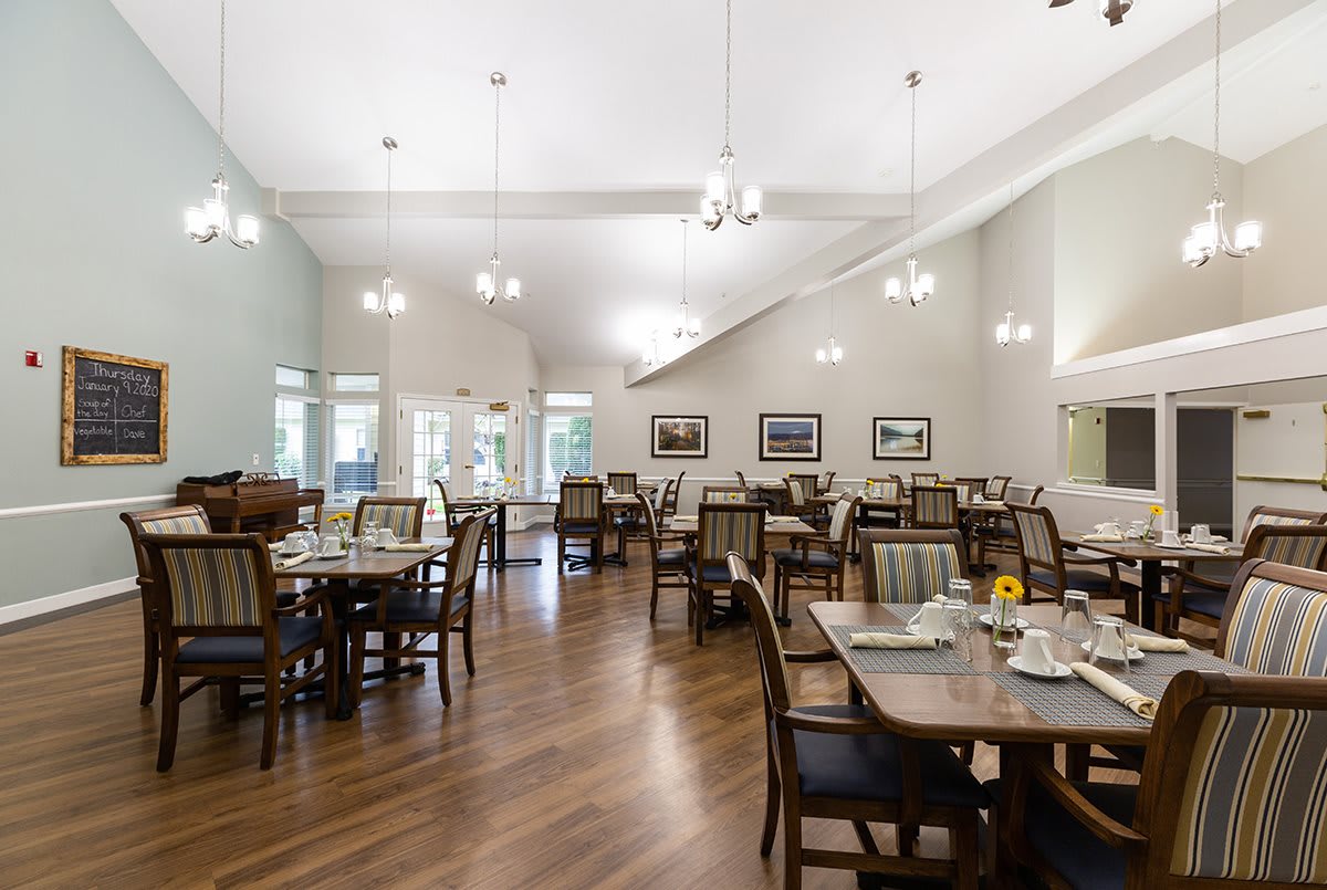 A spacious dining room with neatly arranged tables and chairs, featuring elegant lighting and wooden flooring.