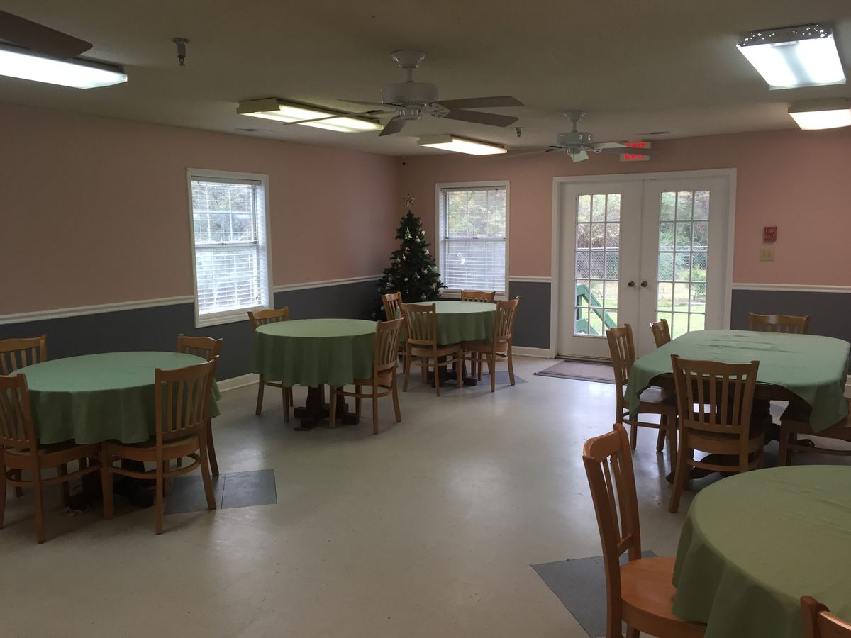 An empty dining room with round tables and chairs arranged neatly, featuring large windows and a simple decor.