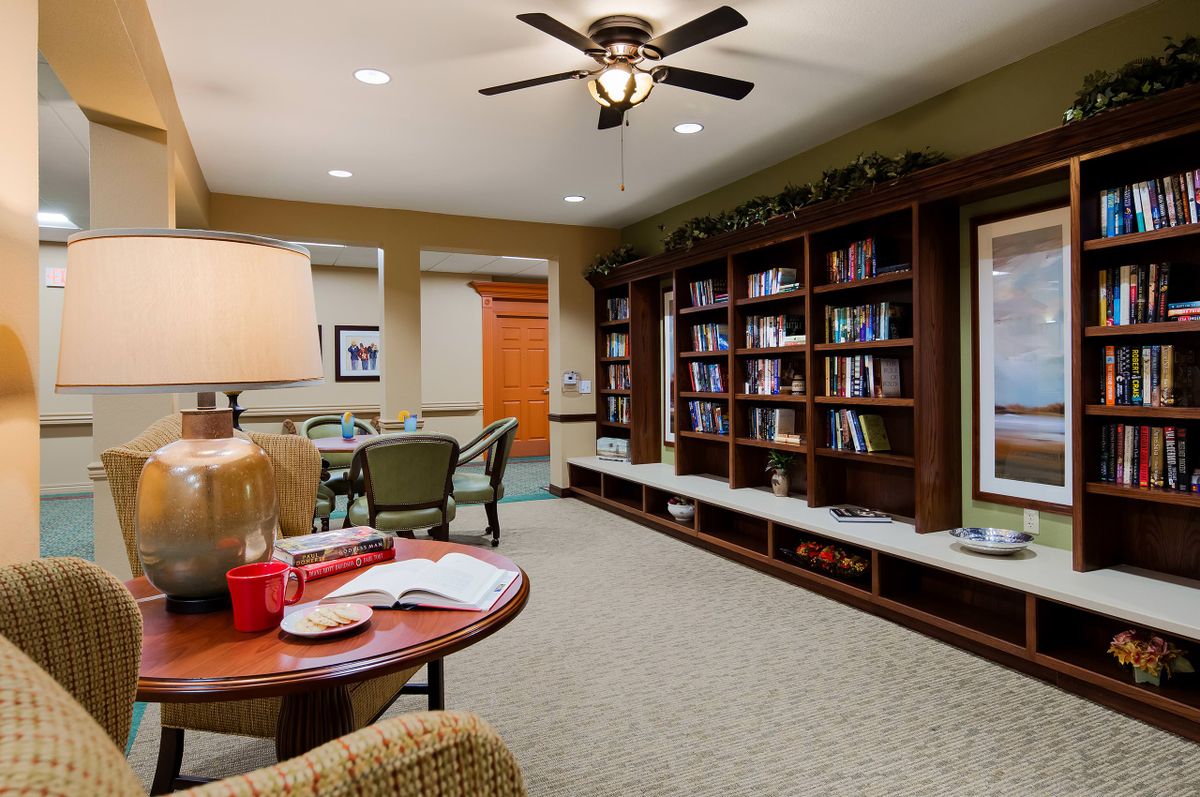 A cozy library room featuring a bookshelf, comfortable seating, and a ceiling fan.