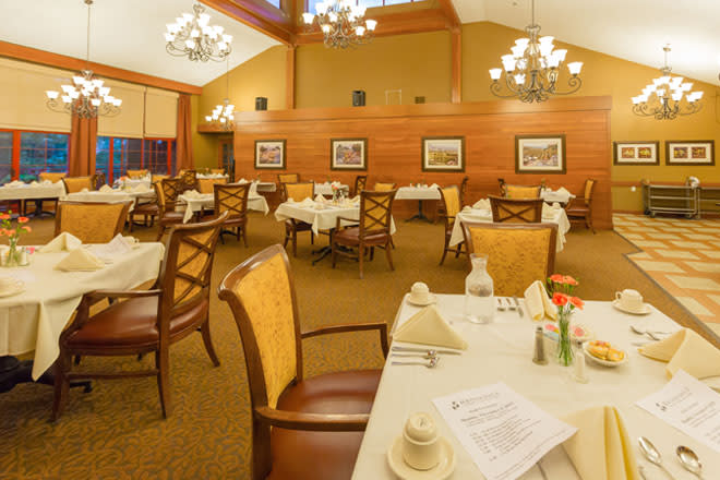 An elegant dining room with neatly arranged tables and chairs, illuminated by chandeliers.
