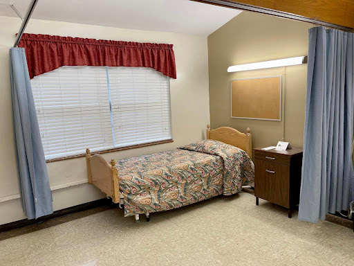 A simple hospital room featuring a single bed, bedside table, and window.