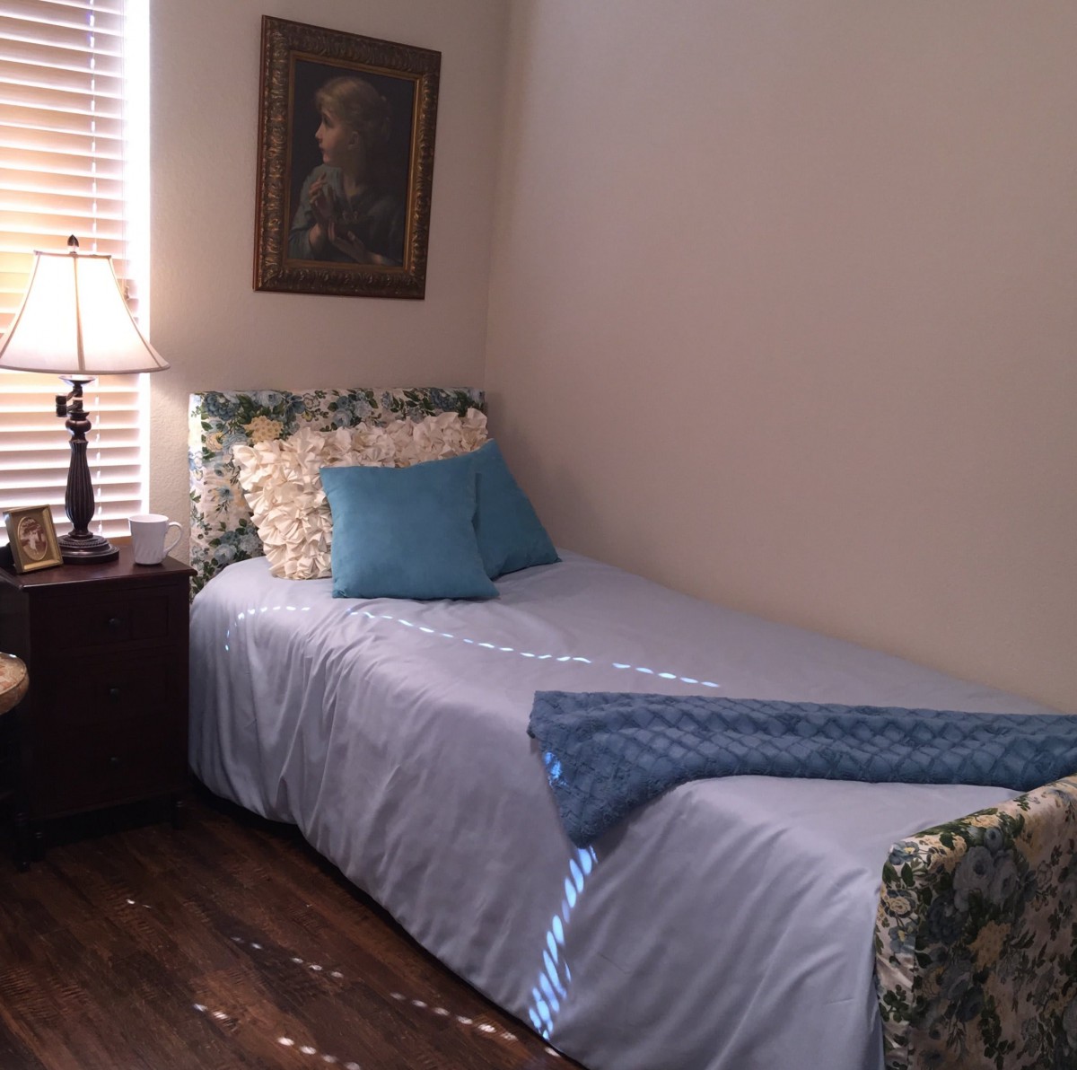 A cozy bedroom with a single bed and decorative pillows beside a nightstand and lamp.