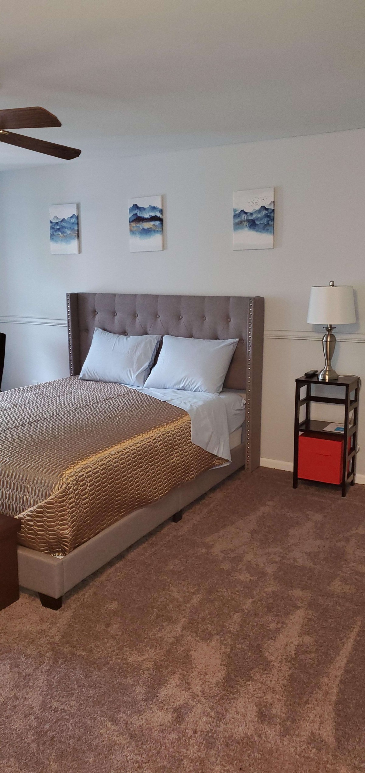A cozy bedroom with a plush bed, nightstand with a lamp, and decorative artwork on the wall.