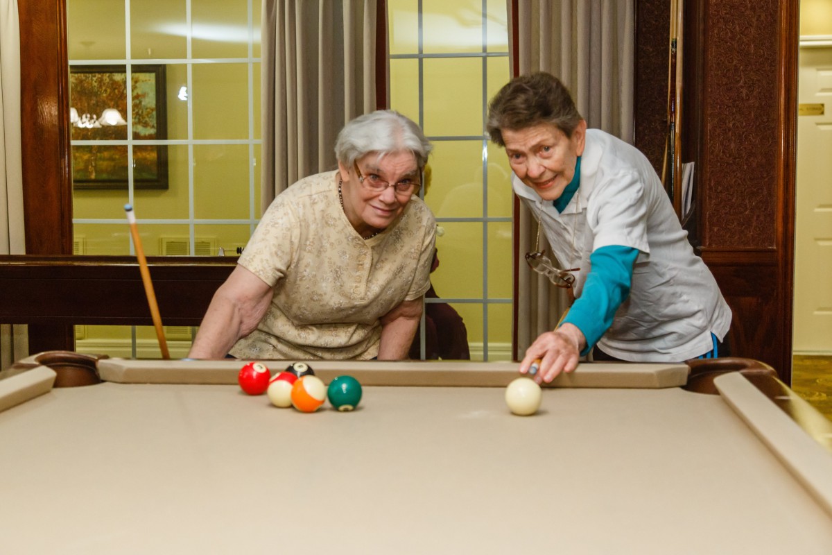 Two elderly people enjoying a game of billiards.