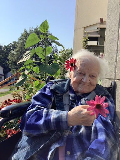 An elderly woman enjoying the beauty of flowers in her garden while sitting in a wheelchair.