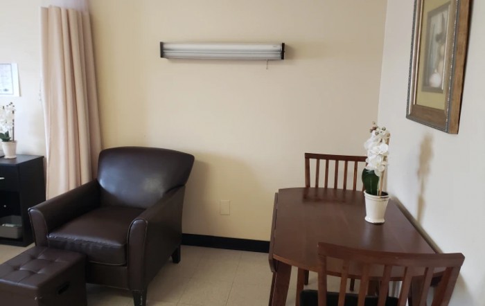 A cozy interior with a dark leather chair, a wooden table and chairs, an overhead light fixture, and a potted orchid.