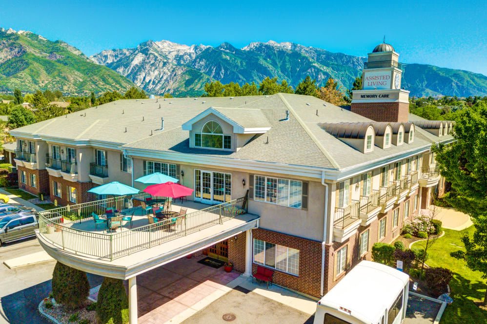 A scenic view of a large building with a patio and colorful umbrellas, set against a backdrop of mountains.