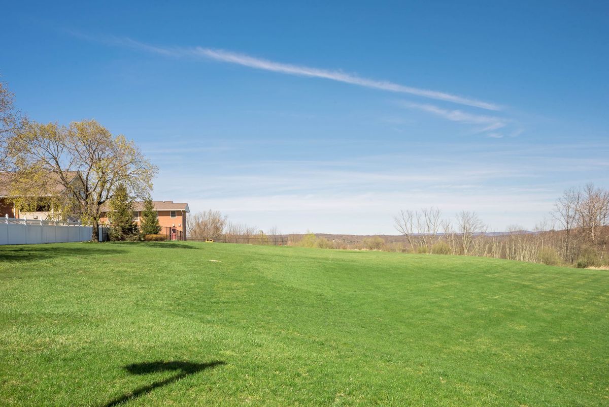 A scenic view of a house on a grassy field under a clear blue sky.
