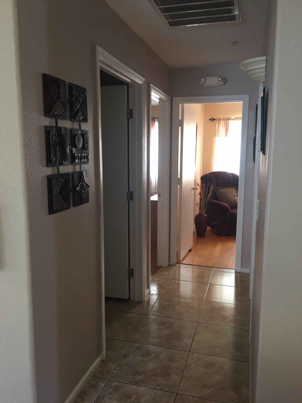 A view down a hallway with doors leading to various rooms, featuring tiled flooring and photographs on the wall.