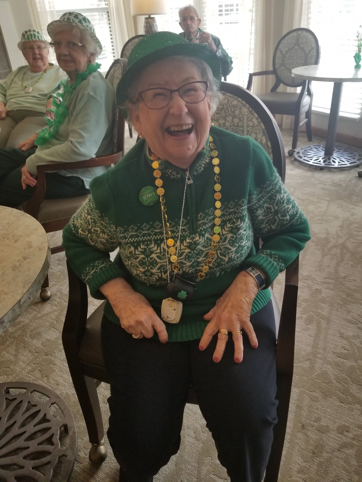 An elderly woman laughing joyfully while dressed in festive green attire and accessories, celebrating St. Patrick's Day.