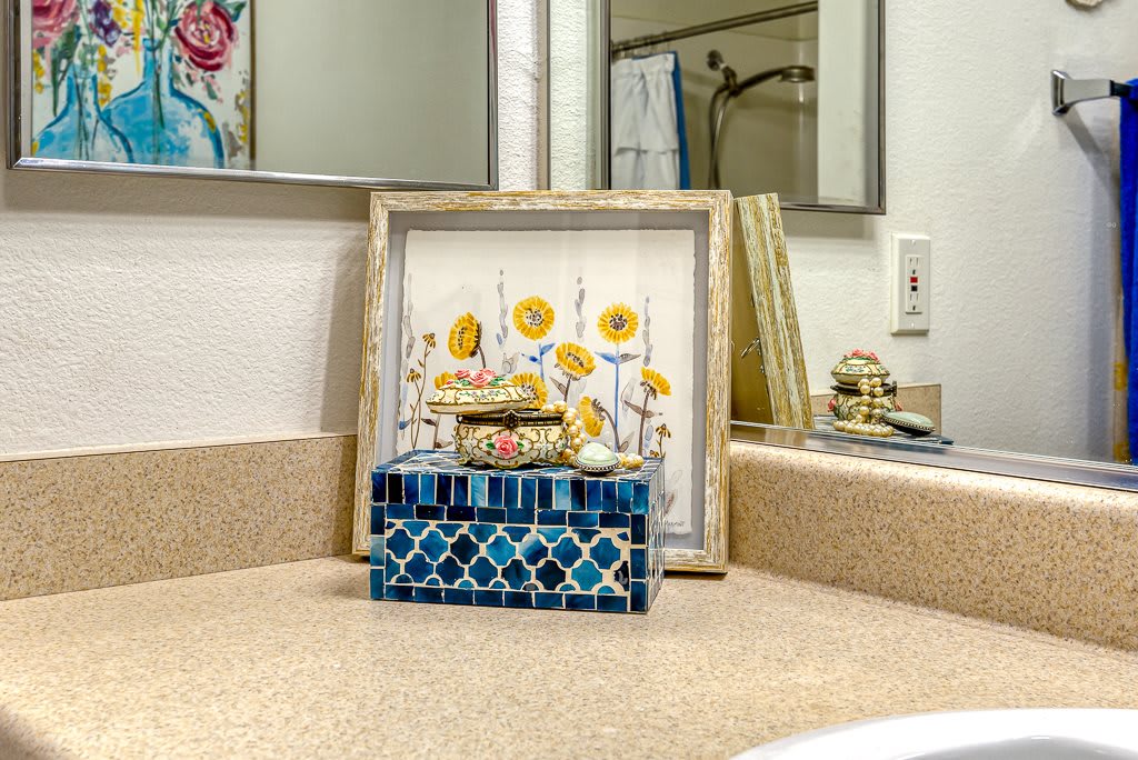 A bathroom countertop adorned with a framed floral artwork and a decorative blue tiled box.