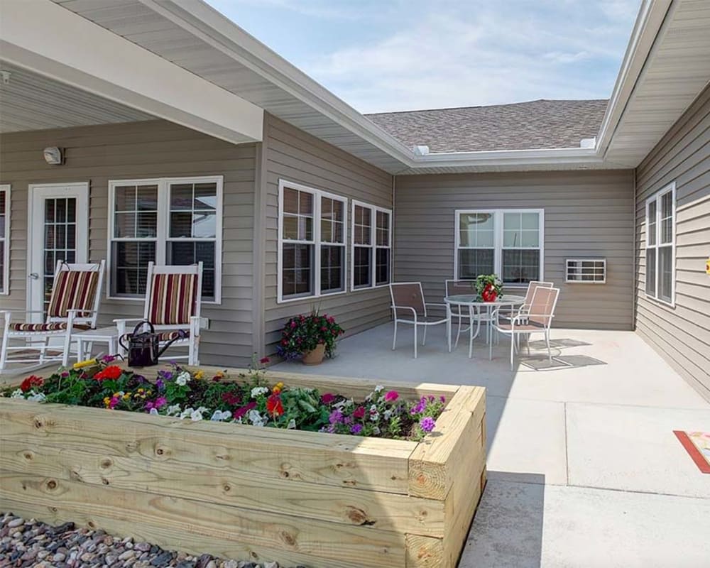A cozy patio area featuring outdoor seating and a wooden flower bed, set against the exterior of a building.