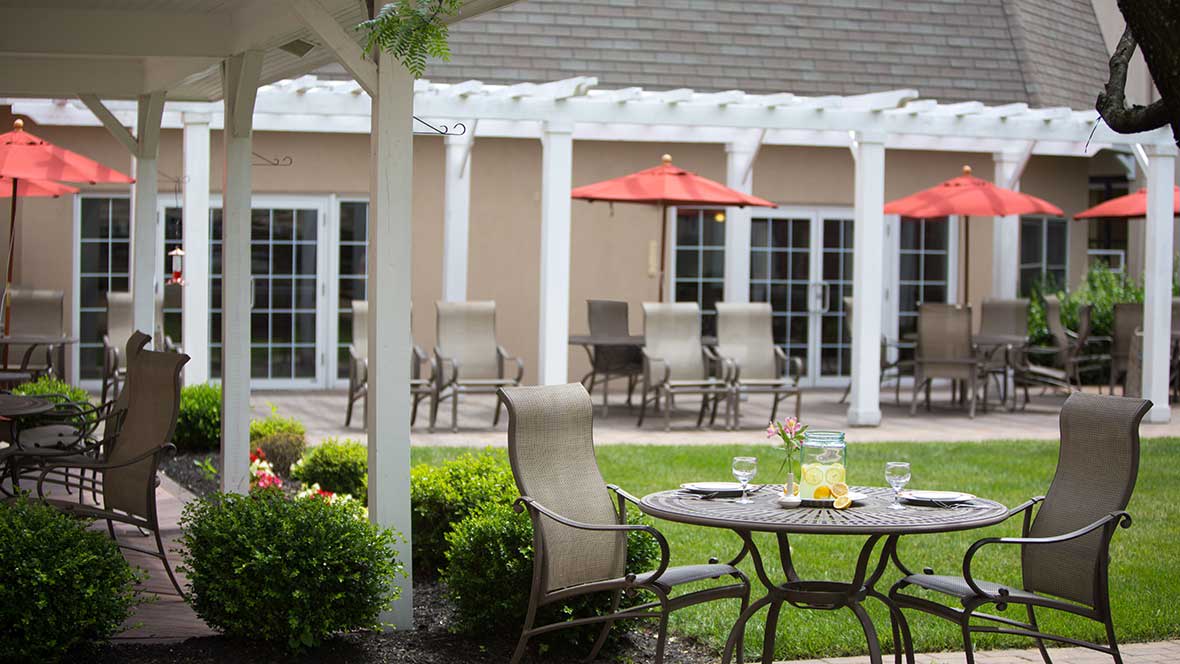 A serene patio setting with outdoor furniture, including a table and chairs, situated in a lush garden.