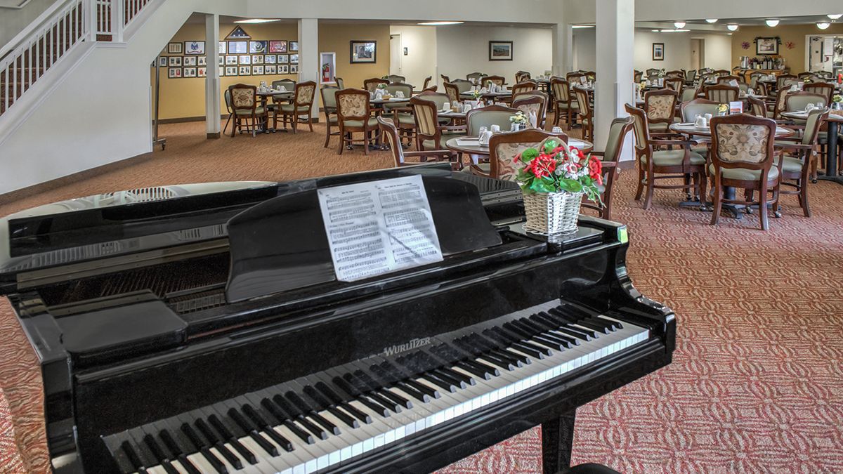 A grand piano in a dining area with tables and chairs.