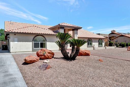 A beautifully designed house with desert landscaping, featuring palm trees and decorative rocks under a blue sky.