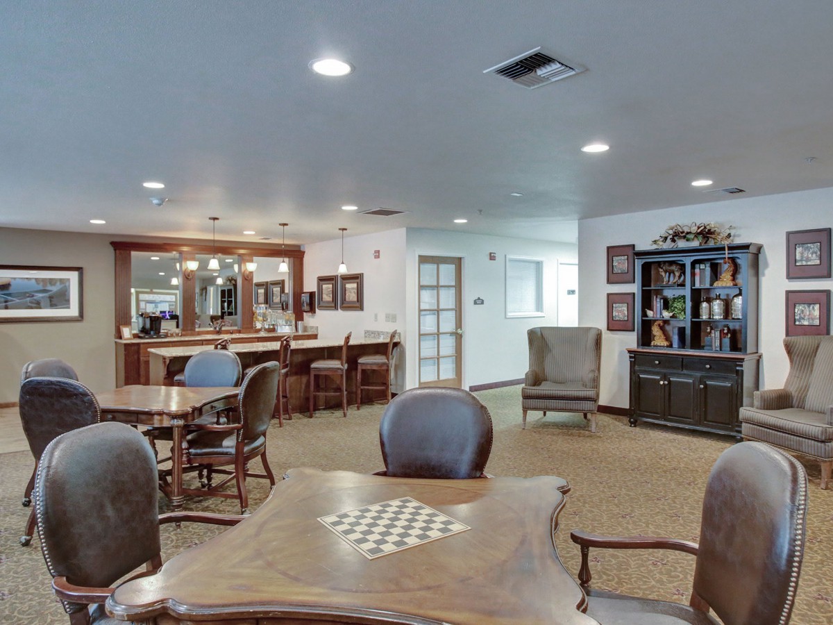 A cozy living room featuring a chess table, comfortable seating, bookshelves, and a bar counter.