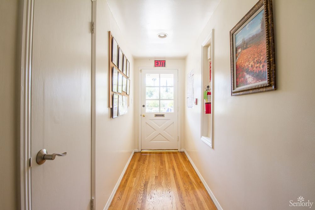 A well-lit hallway with wooden flooring and decorative paintings leading to a door.