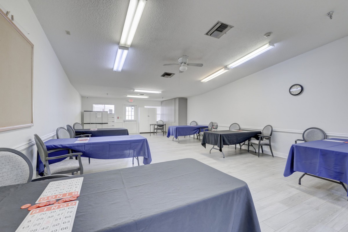 An empty conference room with tables covered in tablecloths, surrounded by chairs and lit by fluorescent lights.