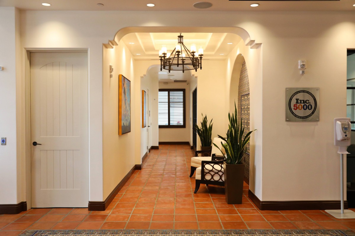 A stylish hallway with archways, a chandelier, and wooden flooring, featuring plants and seating.
