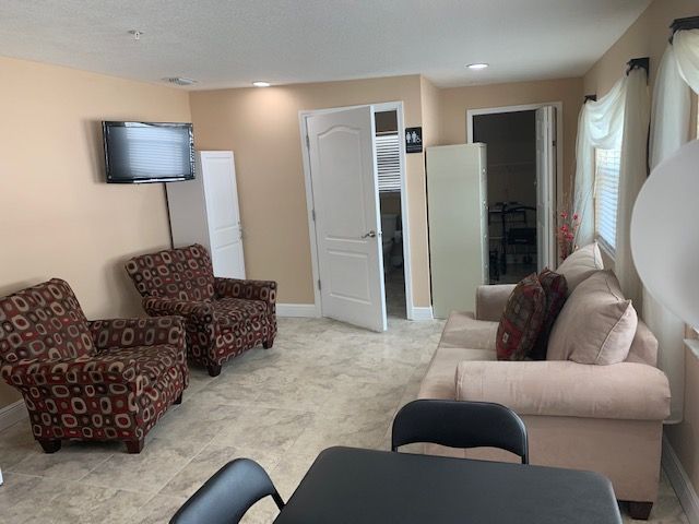 A cozy living room with chairs, a sofa, a table, and a TV mounted on the wall.