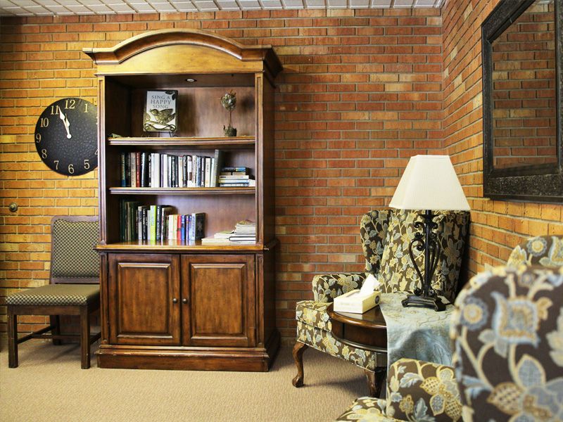 A cozy living room with a wooden bookshelf, armchair, and lamp against a brick wall.