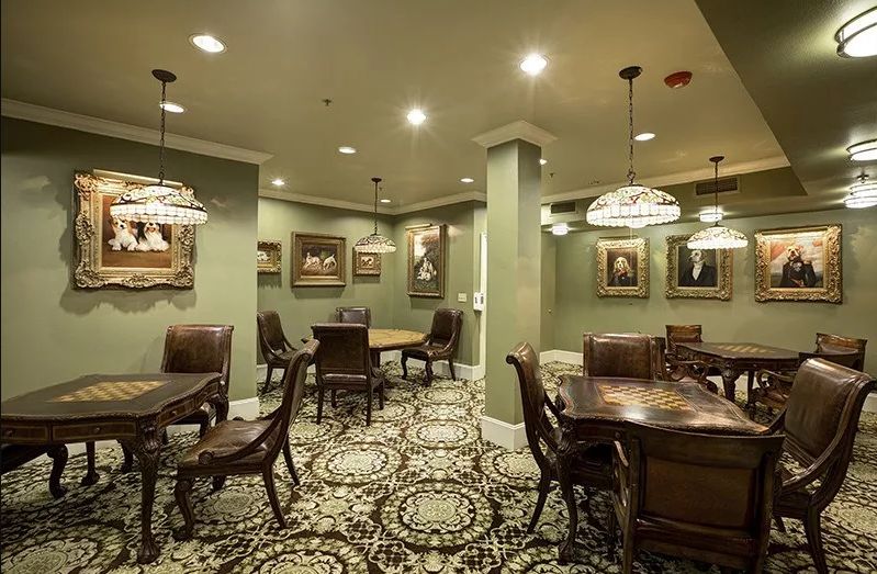 A well-furnished room with multiple tables and chairs, surrounded by paintings and elegant lighting.