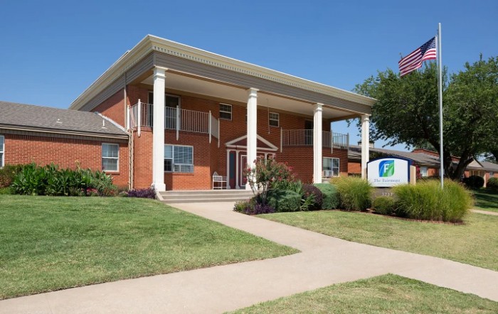 A brick building with large white columns and a well-maintained lawn.
