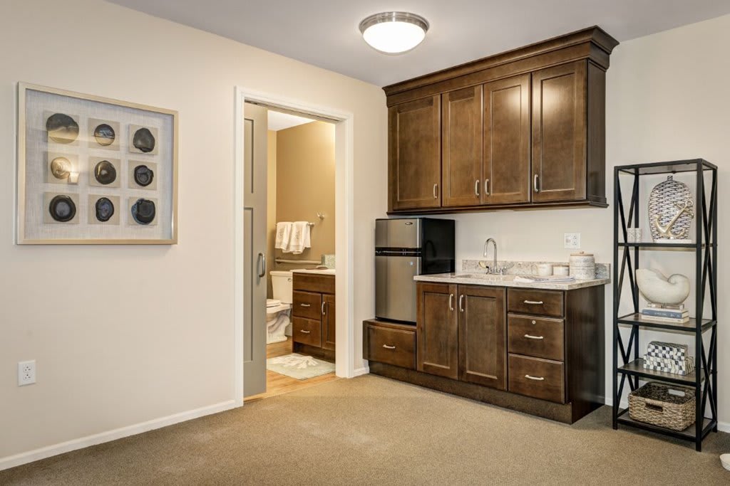 A compact kitchen area with wooden cabinets, a small fridge, and a sink, adjacent to a bathroom.