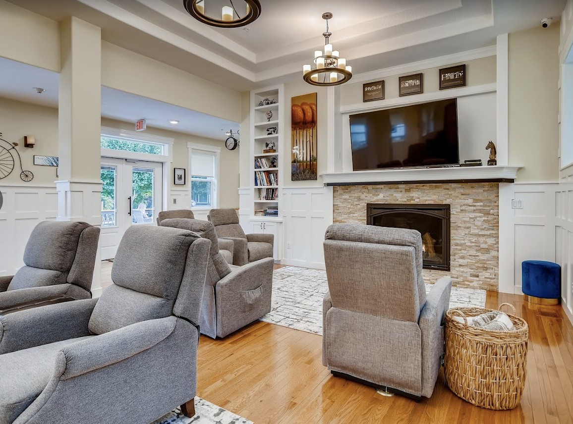 A cozy living room featuring comfortable armchairs, a modern fireplace, and a large television, all set on elegant hardwood flooring.