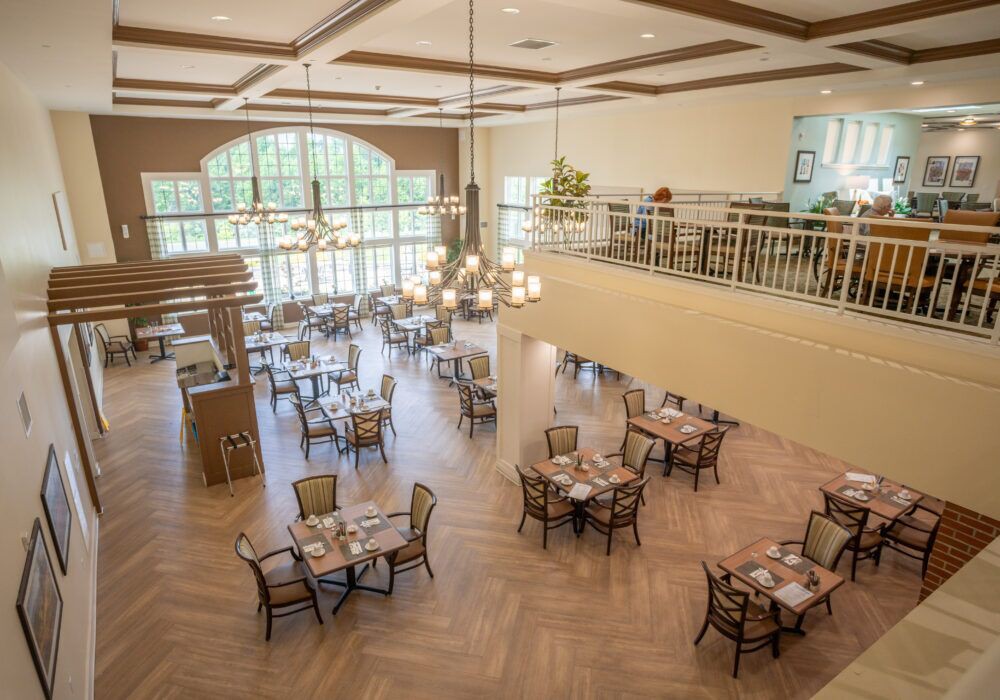 A spacious dining area with elegant chandeliers, multiple tables set for dining, and a balcony overlooking the arrangement.