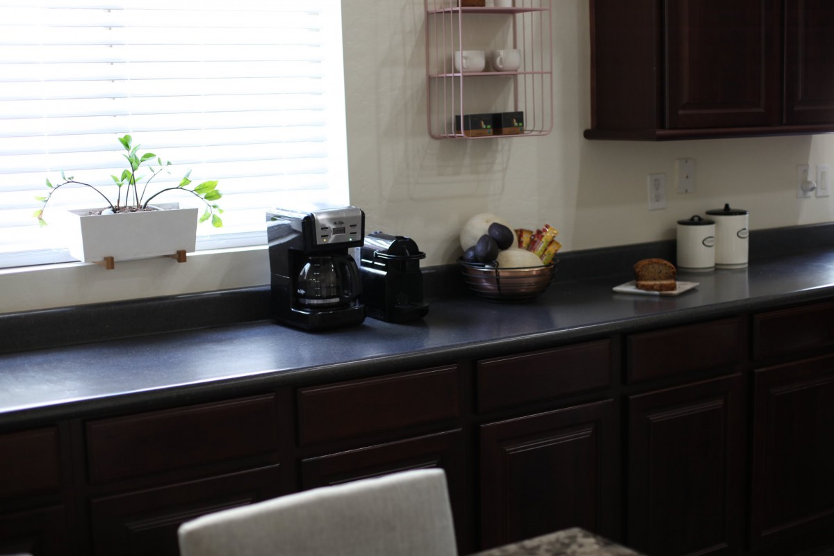 A tidy kitchen countertop with a coffee maker and fruit basket near a window.