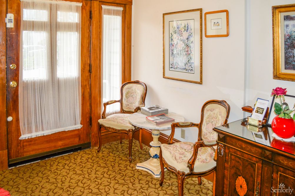 A cozy sitting area with vintage chairs and a small table, featuring wooden doors and framed artwork on the wall.