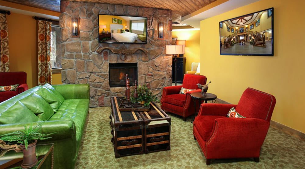 A cozy living room with a stone fireplace, green sofa, red chairs, and a TV mounted above the fireplace.