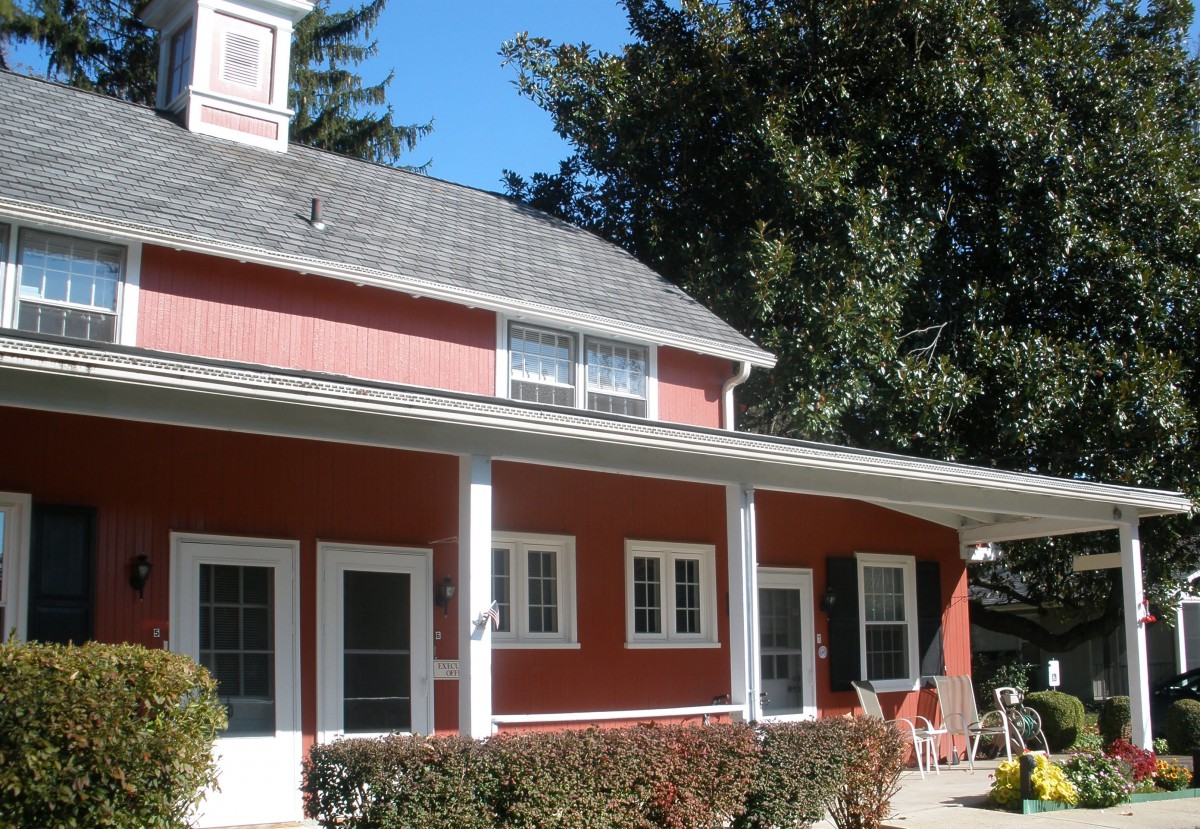 A charming red house with a porch surrounded by trees.