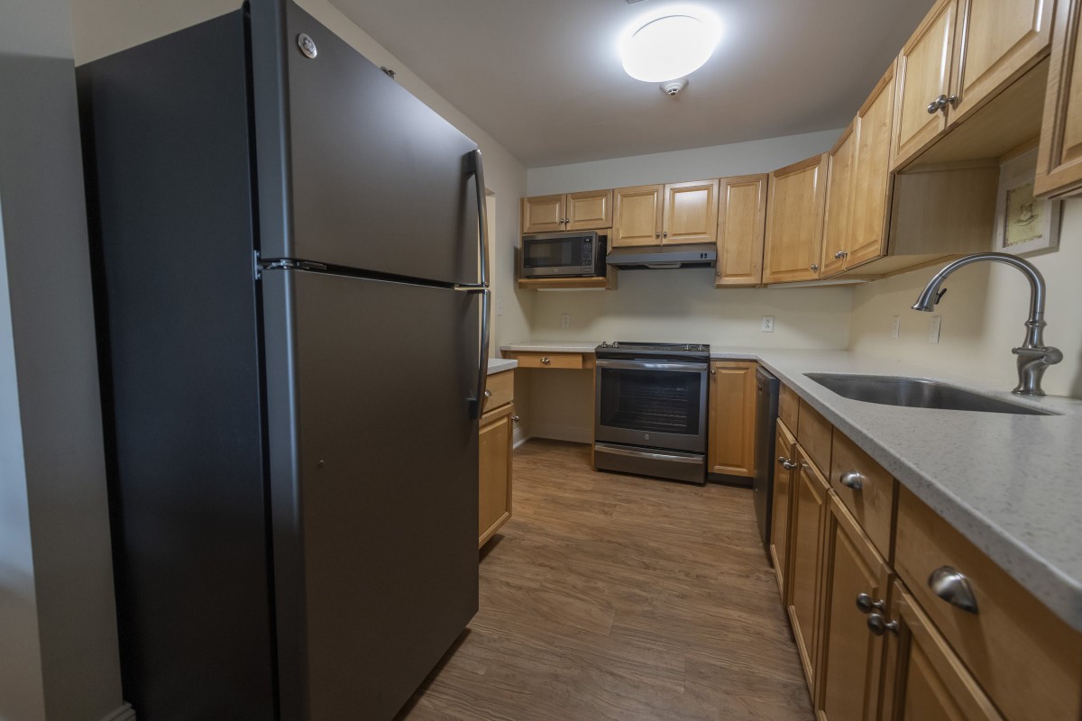 A modern kitchen with wooden cabinets, equipped with a refrigerator, stove, and microwave.