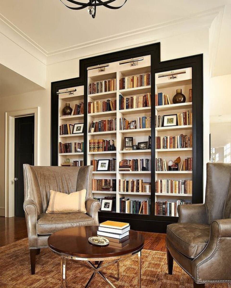 A cozy living room with a large bookshelf, armchairs, and a coffee table.