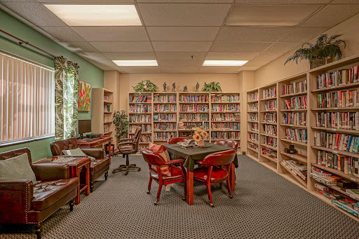 A cozy library space featuring bookshelves filled with books, a central table surrounded by chairs, and a warm atmosphere for studying and reading.