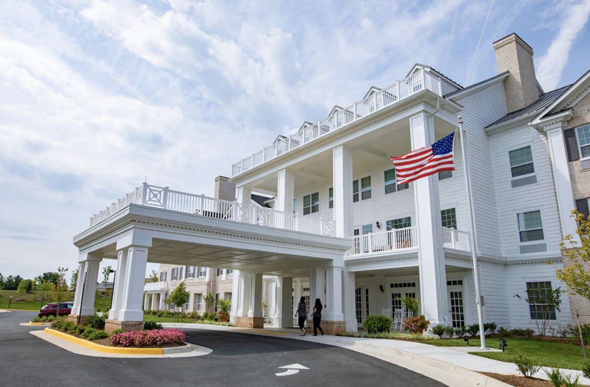 A grand building with columns and flags at the entrance, set against a partly cloudy sky.